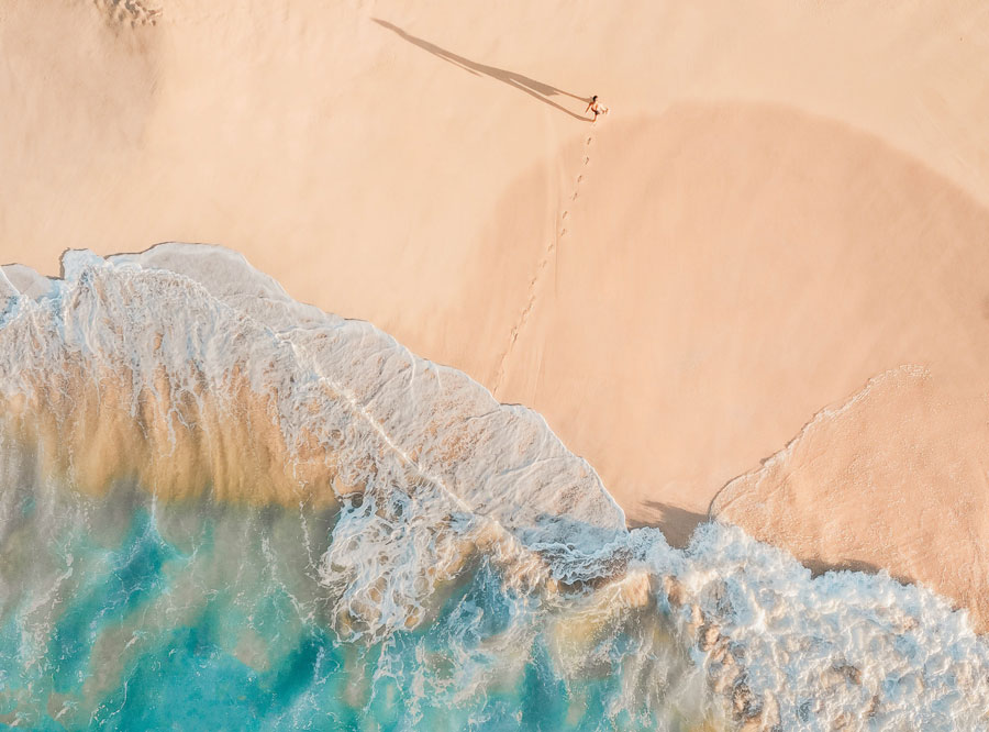 Aerial picture of waves on a beach with a person standing on the beach