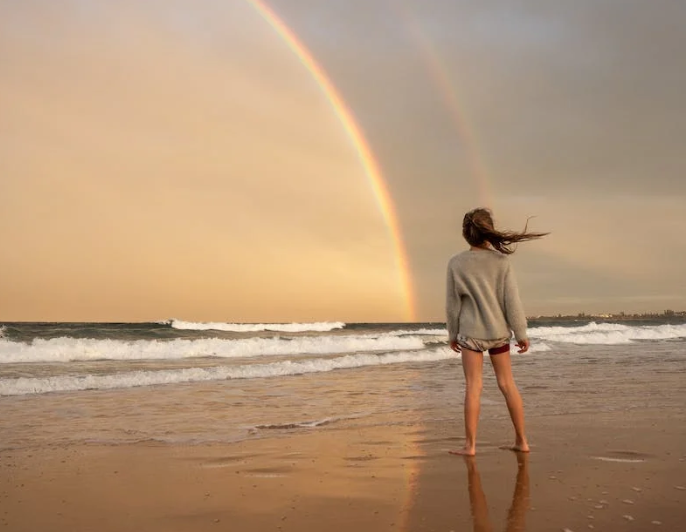 Girl on a beach looking at a rainbow